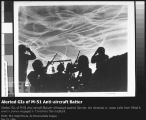1944 – Alerted GIs of M-51 Anti-aircraft Battery silhoutted against German sky streaked w. contrails