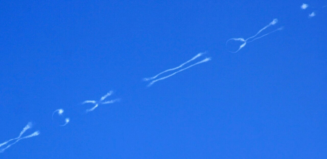 Often mistaken for chemtrails, this is an aircraft contrail displaying Crow instability with looping and wave-like patterns caused by interacting wingtip vortices in the upper atmosphere.